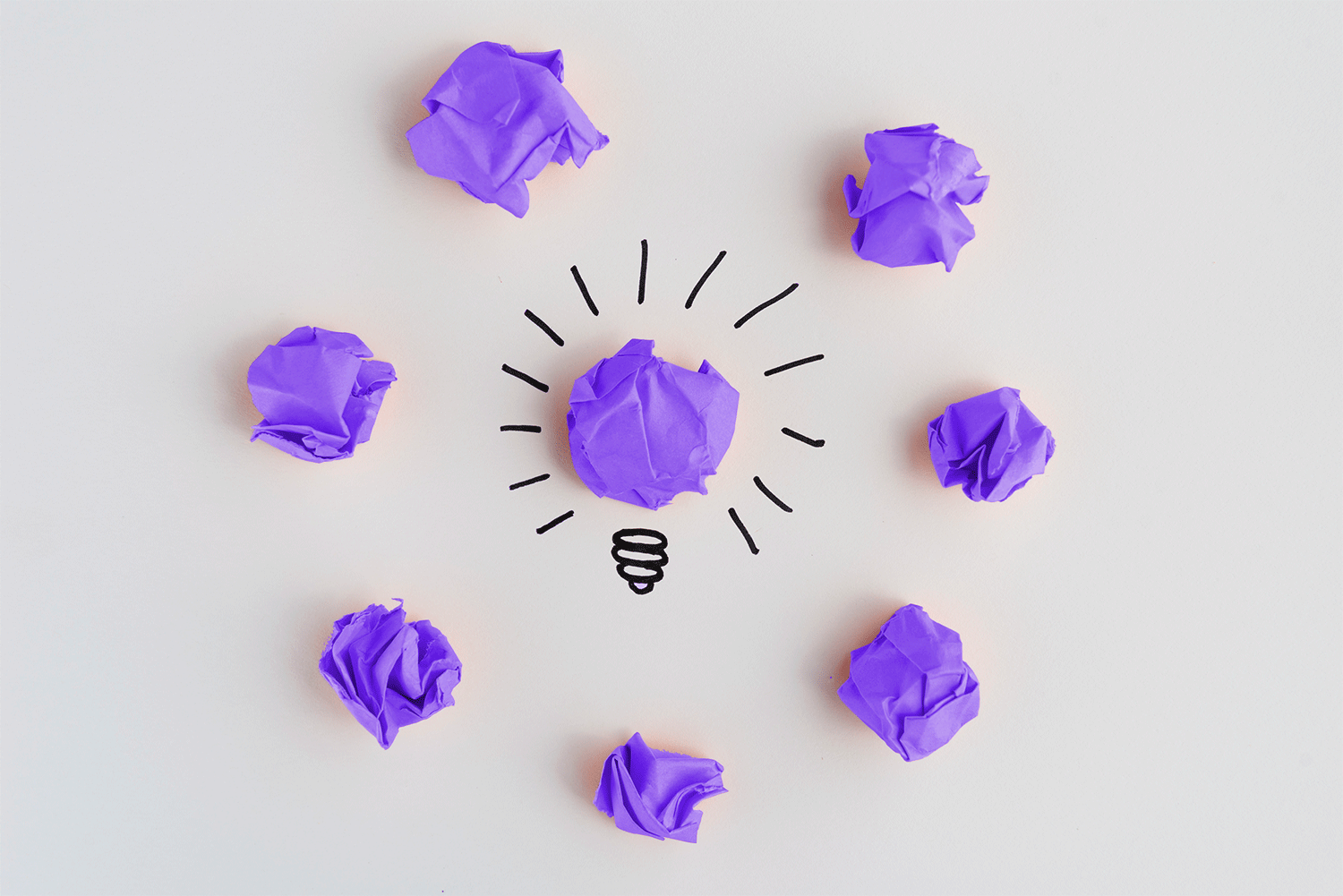 Bombilla rodeada de bolas de papel violeta: ideas con criterio
